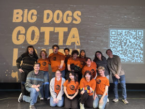 Performers at the Humor Showcase pose together in front of the Big Dogs Gotta Laugh display